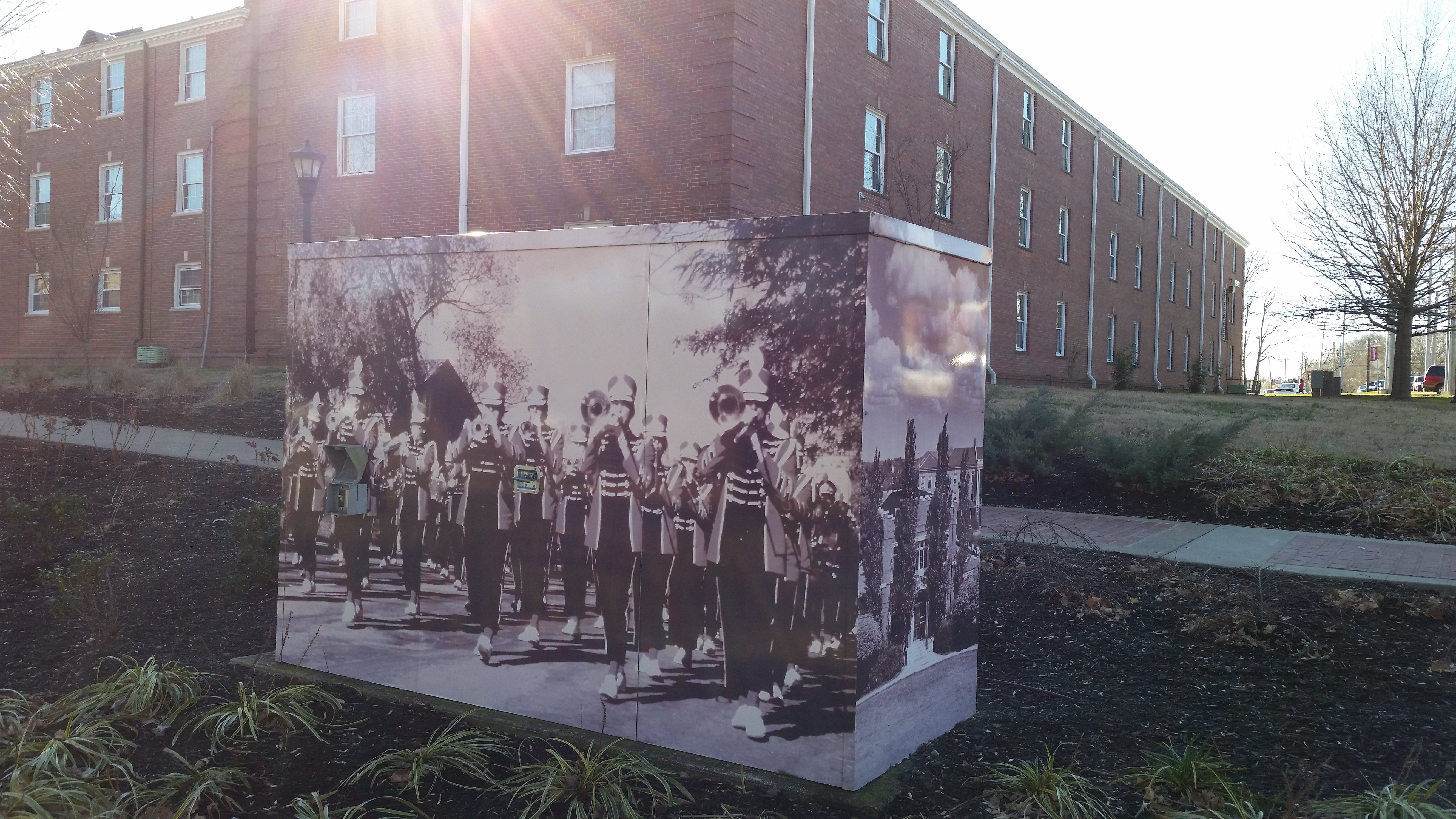 An enclosure in front of a brick building with an image of a marching band vinyl wrap.