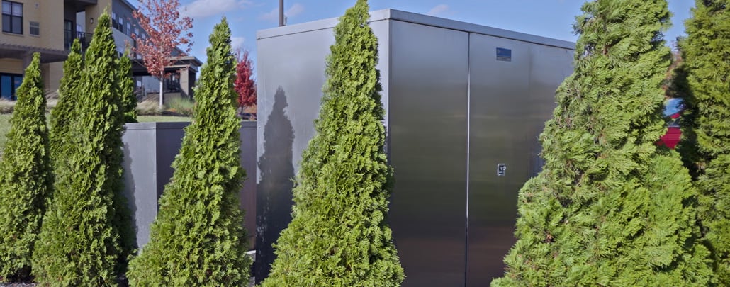 A An aluminum backflow preventer enclosure by Safe-T-Cover surrounded by evergreen tree landscaping.