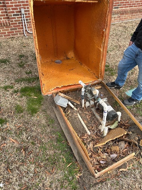 An open fiberglass insulated enclosure with damaged interior walls is no longer protecting the backflow equipment.