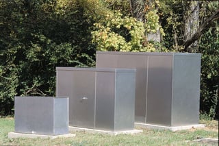 An image of 3 aluminum enclosures of varying sizes sitting side by side. One enclosure is used as a backflow enclosure.