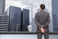 Composite image of businessman standing with hands behind back on the roof of building watching the city.jpeg