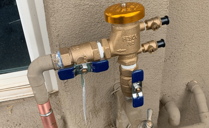 A residential pressure vacuum breaker installed outside a house