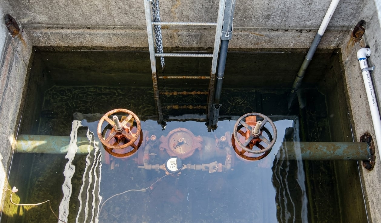 A flooded precast concrete utility vault with backflow preventer equipment submerged